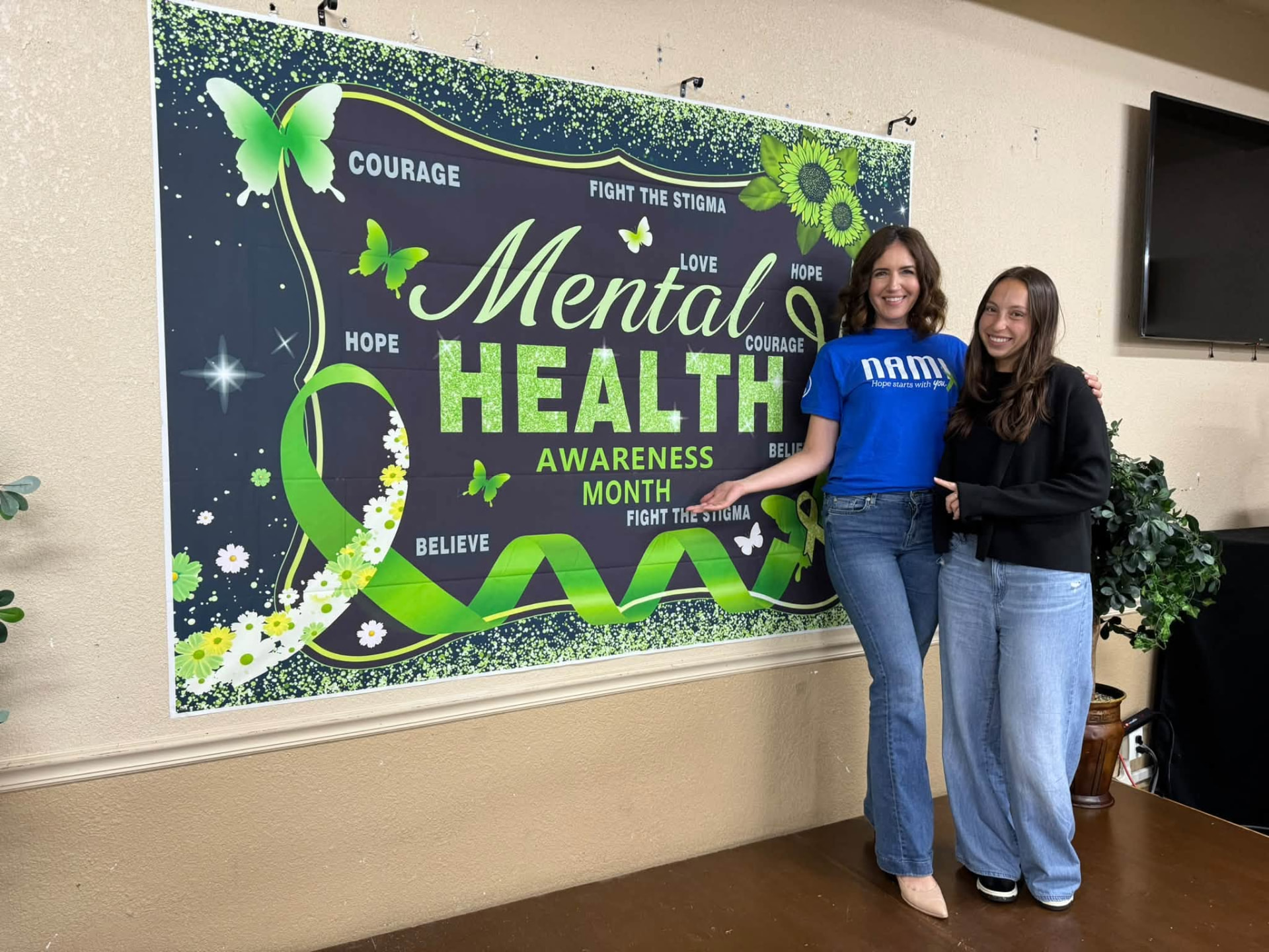 Erika Marcus and a fellow advocate smiling beside a Mental Health Awareness Month banner