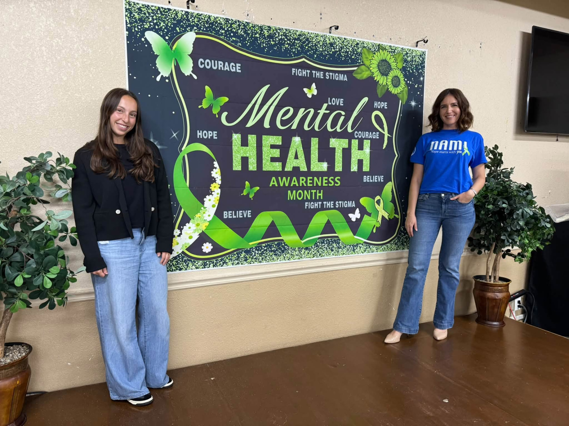 Two women standing either side of a Mental Health Awareness Month banner on stage
